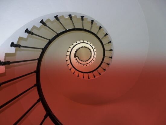 Kręcone schody (widok z dołu na górę), na obraz naniesione biało-czerwone barwy.
